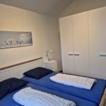 Zimmer mit Doppelbett, Kleiderschrank und Wandbild mit Kitesurfern.