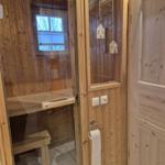 Sauna mit Holzwand, Sitzbank und Fenster. Tür mit Hausanhänger und Toilettenpapierhalter.