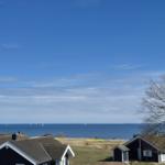 Meeransicht mit Segelbooten und Häusern im Vordergrund unter blauem Himmel.