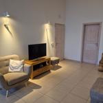 Wohnzimmer mit Sessel, Fernseher und Holztisch. Zwei Türen und dekorative Vasen sind sichtbar.