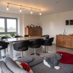 Essbereich mit Tisch und Stühlen, Sofa mit Kissen und Decke, Fenster mit Blick auf Feld.