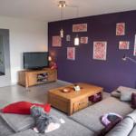 Wohnzimmer mit lila Wand, Sofa, Couchtisch und Fernseher.