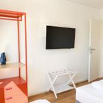 Schlafzimmer mit Bett, Kleiderschrank und Fernseher. Tür führt in Wohnbereich.