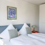 Schlafzimmer mit Bett, Kissen, Nachttisch und Wandbild.