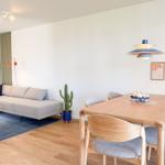 Wohn- und Essbereich mit Sofa, Tisch und Stühlen. Wandlampe und Pflanze sind sichtbar.