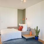 Schlafzimmer mit Bett, Sofa, Kaktus und Holzboden. Tür führt in einen angrenzenden Raum.