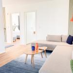 Wohnzimmer mit Sofa, Couchtisch und Fernseher. Blick in Schlafzimmer und Bad.
