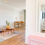 Wohnbereich mit Sofa, Esstisch und Spiegel. Pinkes Garderobenregal vorne.