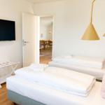 Zwei Betten mit weißen Laken, goldene Deckenleuchten und Fernseher an der Wand.