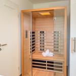 Eine Sauna mit Holzwand, Sitzbank und Handtuch. Die Tür ist offen.