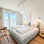 Schlafzimmer mit Doppelbett, Schreibtisch und Fensterblick auf Wohngebiet.