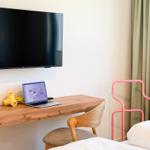 Schreibtisch mit Laptop, Fernseher und Bett