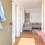Eingangsbereich mit Jeansjacke, rosa Bank und Blick in Wohnzimmer mit Sofa.