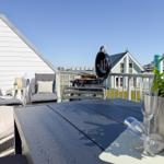 Terrasse mit Tisch, Stühlen, Grill und Pflanze. Blick auf Haus und Grünfläche.