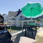 Terrasse mit Grill, Tisch, Stühlen und grünem Sonnenschirm. Hintergrund: Wohnhäuser.