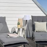 Zwei Liegestühle mit Kissen stehen auf einer Terrasse vor einer weißen Wand.