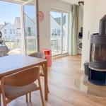 Esszimmer mit Holztisch, Stühlen und Kaminofen. Durchgang zur Terrasse mit Blick auf Nachbarhäuser.