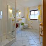 Badezimmer mit Dusche, Waschbecken und Toilette. Fenster mit gelben Vorhängen.