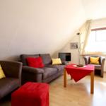 Wohnzimmer mit Sofa, Sessel und Tisch unter Dachschrägen.