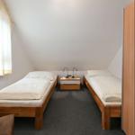 Zwei Einzelbetten mit Nachttisch und Lampen in einem Dachzimmer mit Fenster und Kleiderschrank.