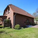 Ein rotes Backsteinhaus mit Dach und Garten. Links steht ein Schaukelstuhl.