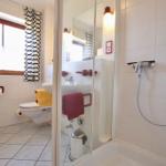 Badezimmer mit Dusche, Toilette und Waschbecken. Fenster mit Vorhängen.