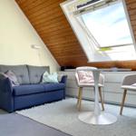 Ein Wohnraum mit Sofa, Tisch und Stühlen unter einer Dachschräge mit Fenster.