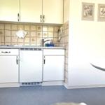 Küche mit weißen Schränken, Fliesenwand und Arbeitsplatte. An der Wand hängen zwei Bilder.
