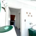 Schlafzimmer mit grünem Nachttisch und Spiegel. Durchgang zu Wohnbereich mit Holzwand.