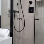 Dusche mit Glaswand, weiße Handtücher und schwarze Armaturen.