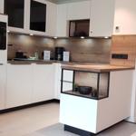 Moderne Küche mit Arbeitsplatte, Schränken und integriertem Ofen. Wohnbereich mit Sofa und Essbereich sichtbar.
