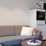 Ein grauer Sofa mit flauschigen Kissen und eine moderne Küche im Hintergrund.