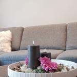 Grauer Sofa mit Fellkissen und Tisch mit Kerzen und Blumen