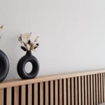 Schwarze Vasen mit getrockneten Pflanzen auf einem Holzkopfteil.