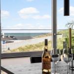 Tisch mit Weinflasche und Gläsern vor großem Fenster mit Meerblick.