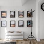 Eingangsbereich mit Bildern an der Wand, Hocker, Kleiderständer und Wanduhr.