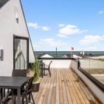 Terrasse mit Tisch und Stühlen, Blick auf Meer und Strand.
