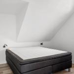 Schlafzimmer mit Doppelbett, Holzboden und Dachschrägen. Fenster mit Pflanze.