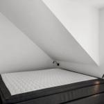 Schlafzimmer mit Dachschrägen, weißer Matratze und schwarzem Bettgestell.