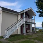 Zweistöckiges Haus mit Balkon und Außentreppe. Blick aufs Meer im Hintergrund.