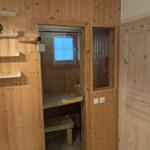 Sauna mit Holzwand, Sitzbank und Fenster. Orange Haartrockner auf Regal.