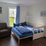 Schlafzimmer mit Bett, Sessel und Glastür zum Garten.