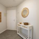 Eingangsbereich mit weißem Tisch, runden Spiegel und Holzgarderobe an der Wand.