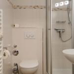 Badezimmer mit Dusche, Toilette und Waschbecken. Weiße Fliesen und Handtuchheizung.