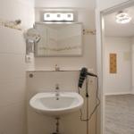 Badezimmer mit Waschbecken, Spiegel und Haartrockner. Blick in angrenzenden Raum.
