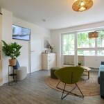 Wohnzimmer mit Sofa, grüner Sessel, TV und großem Fenster.