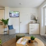 Wohnzimmer mit TV, Pflanzen und Sitzgelegenheiten. Große Fensterfront mit Blick nach draußen.