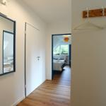 Flur mit Spiegel, Kleiderhaken und Blick in Schlafzimmer mit Bett und Fenster.