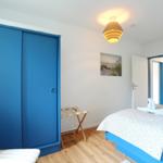Schlafzimmer mit blauem Schrank, Bett und Holzboden. Deckenleuchte und Wandbild sind sichtbar.