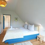 Schlafzimmer mit blauem Bett, Holzboden und schräger Decke. An der Wand hängt ein Bild.